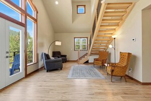 A spacious room with a wooden staircase, a large window, and a view of the outdoors. - Private 22 Acre Farmhouse with Hot Tub and Games (Coeur d'Alene)