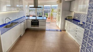 Une cuisine moderne avec des meubles blancs, un plan de travail bleu et une vue sur la ville grâce à de grandes fenêtres.