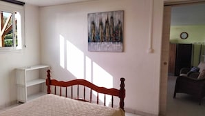 A bedroom with a bed, a radiator, a painting, and a view of a balcony. - Le Ti Colibri **vast T2 gite A FEW STEPS AWAY FROM L'ILET AUX IGUANES! (Le Robert)