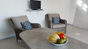 A modern living room with two armchairs, a coffee table, and a television mounted on the wall. - Le Ti Colibri **vast T2 gite A FEW STEPS AWAY FROM L'ILET AUX IGUANES! (Le Robert)