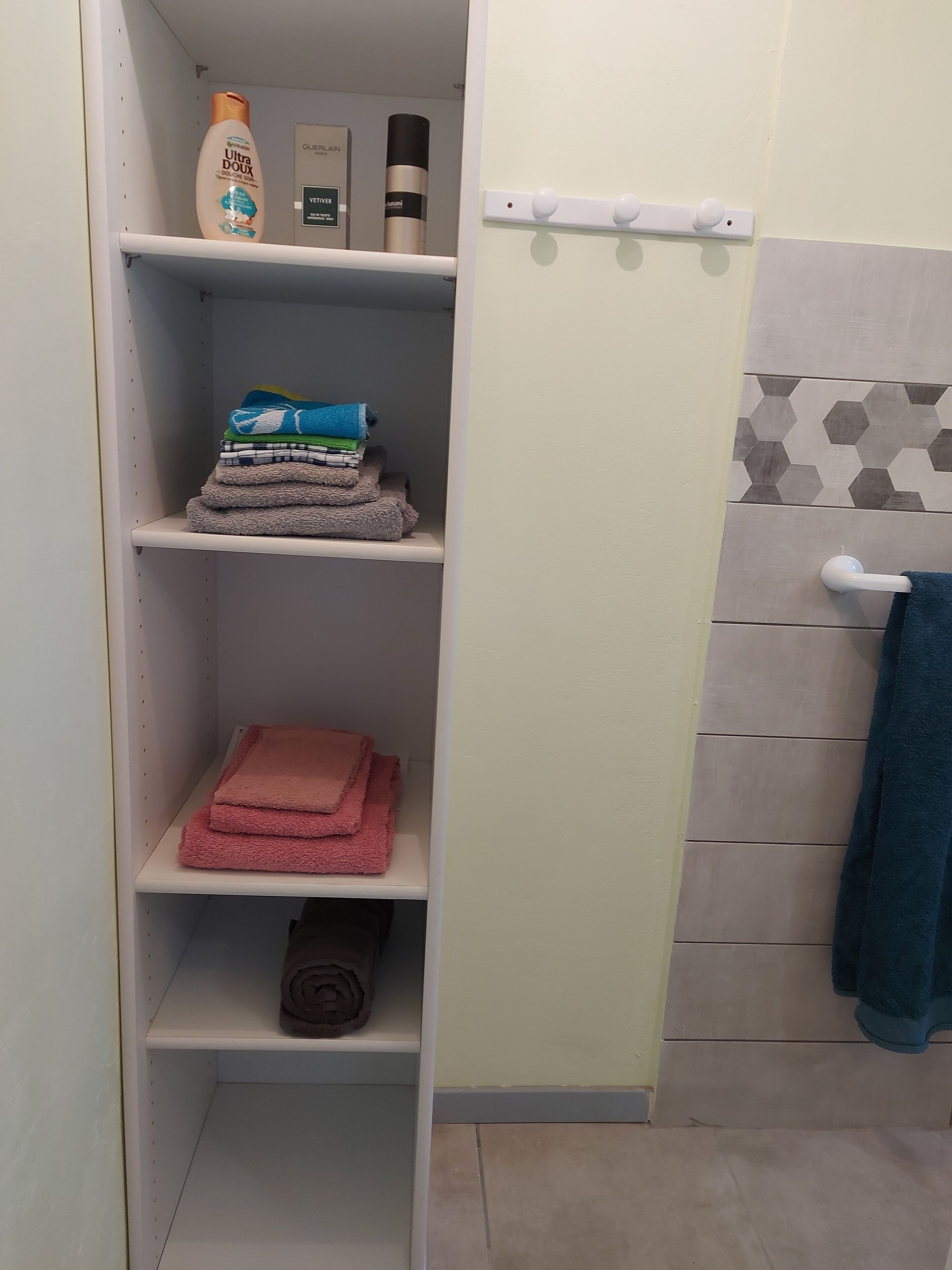 Een badkamer met een plank waarop toiletartikelen, handdoeken en een handdoekhouder met een blauwe handdoek staan.