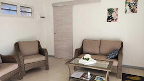 A living room with two armchairs, a sofa, a glass coffee table, and a door. - Le Ti Colibri **vast T2 gite A FEW STEPS AWAY FROM L'ILET AUX IGUANES! (Le Robert)