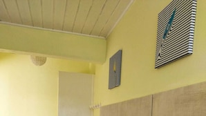 A bathroom with a yellow wall, a white door, and a tiled floor. There are three white towel racks on the wall and a trash can with a green lid. - Le Ti Colibri **vast T2 gite A FEW STEPS AWAY FROM L'ILET AUX IGUANES! (Le Robert)