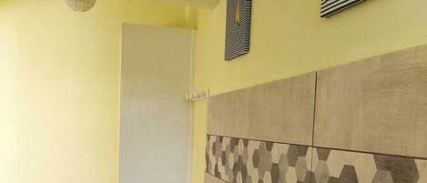 A bathroom with a yellow wall, a white door, and a tiled floor. There are three white towel racks on the wall and a trash can with a green lid.