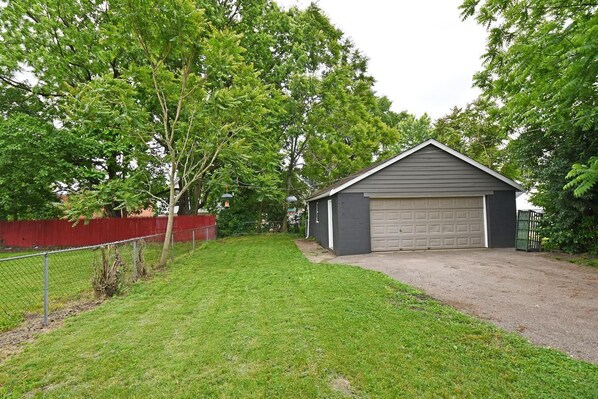 Residential garage situated in a grassy yard with a red fence and trees in the background.