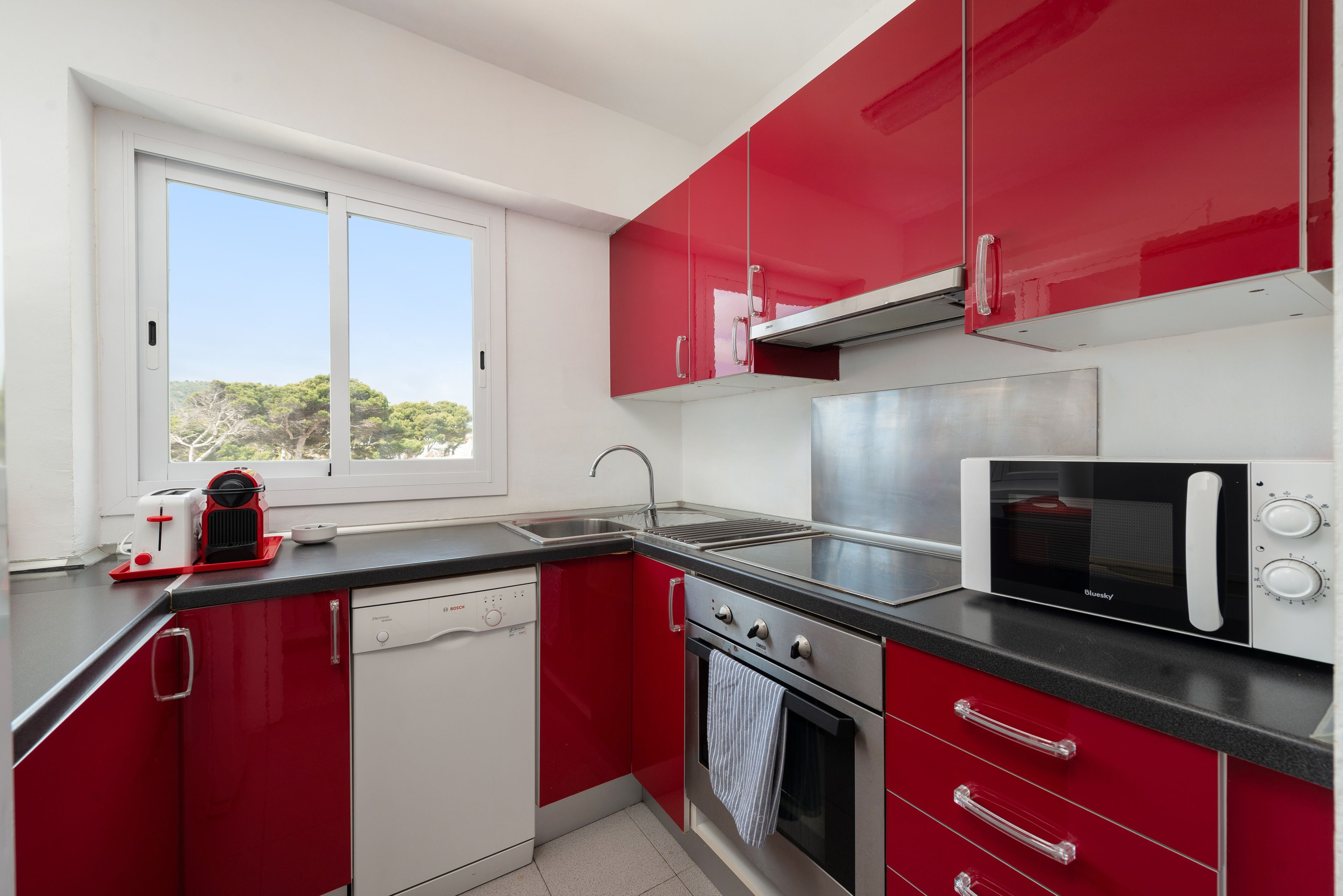 A compact kitchen with red cabinets, a dishwasher, a stove, and a microwave.