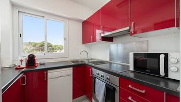 A compact kitchen with red cabinets, a dishwasher, a stove, and a microwave.