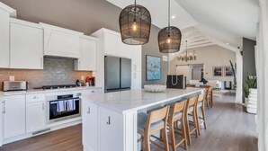 A modern kitchen with white cabinetry, a large island with bar stools, and pendant lighting. - Newly Renovated, Modern home with pool, cathedral ceilings, open-floor... (Southampton)
