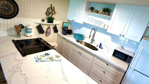 A modern kitchen with a marble countertop, a built-in oven, a microwave, and a refrigerator. - Pheapie Beach Retreat, Beachfront, W/ Air Conditioner, Large Lanai (Hauula)
