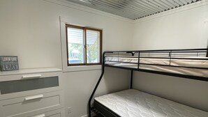 Ein Etagenbett mit Matratze, ein Schreibtisch mit Schubladen, ein Fenster und ein Schild auf dem Schreibtisch.
