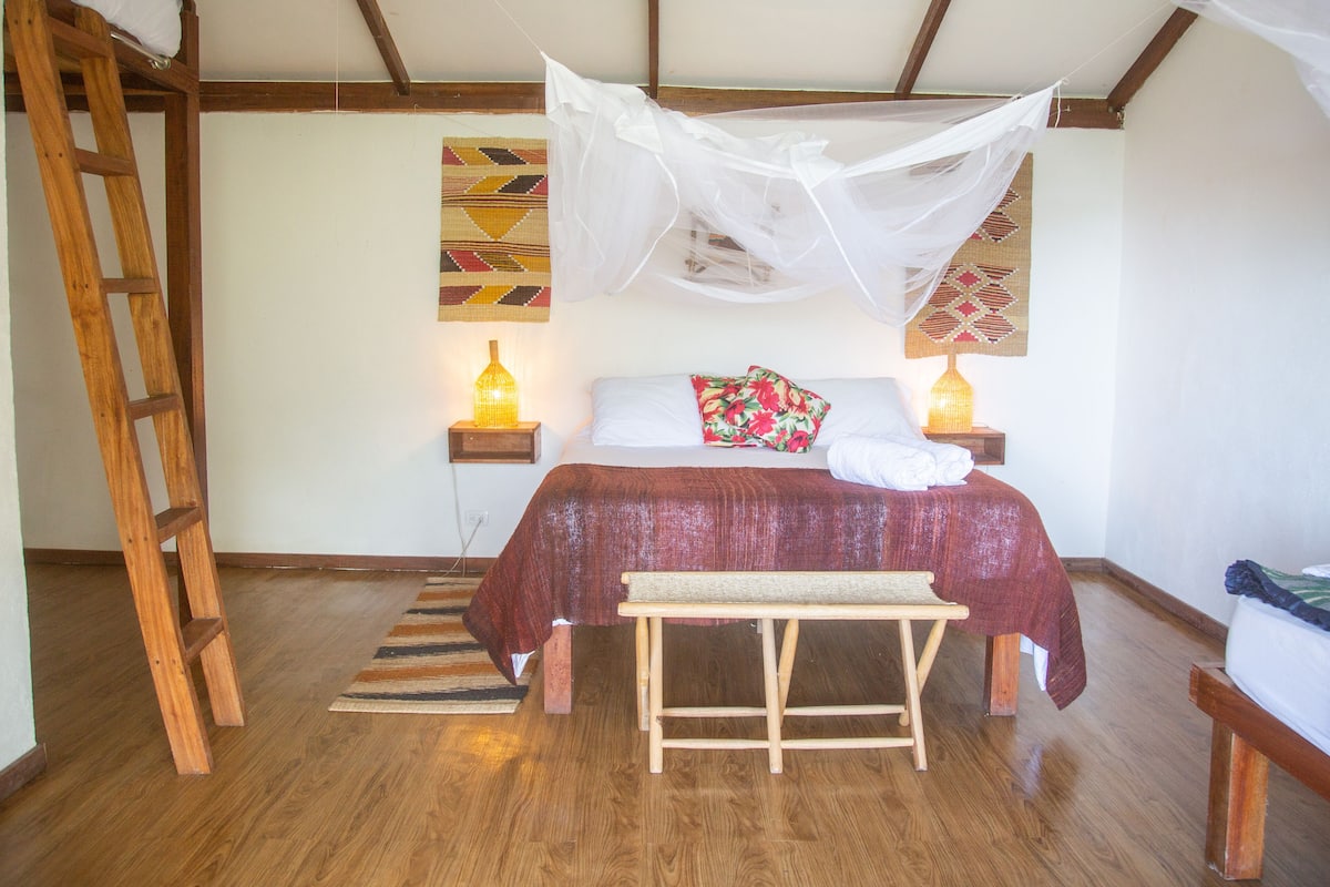 A room with a bed, a wooden ladder, a bench, and two wall-mounted lamps.
