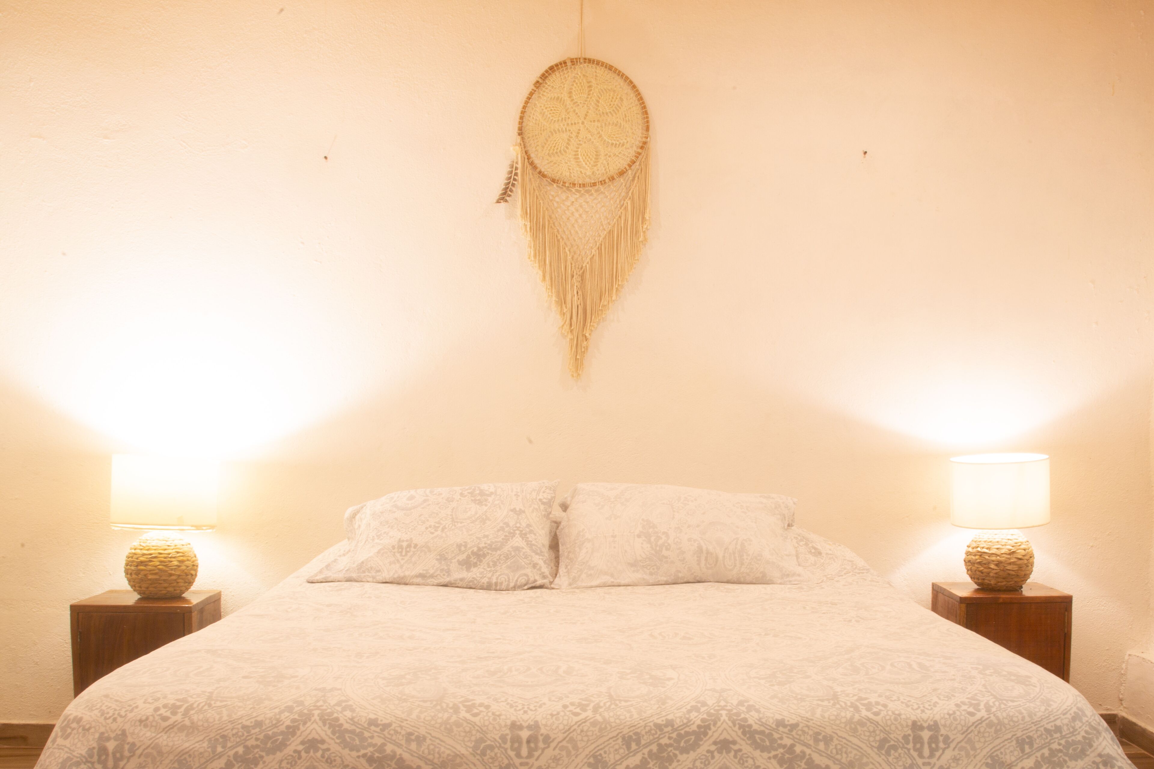 A bed with a patterned bedspread, two bedside lamps, and a hanging dreamcatcher.