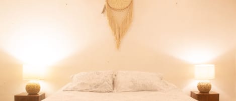 Una cama con una colcha estampada, dos lámparas de noche y un atrapasueños colgante.