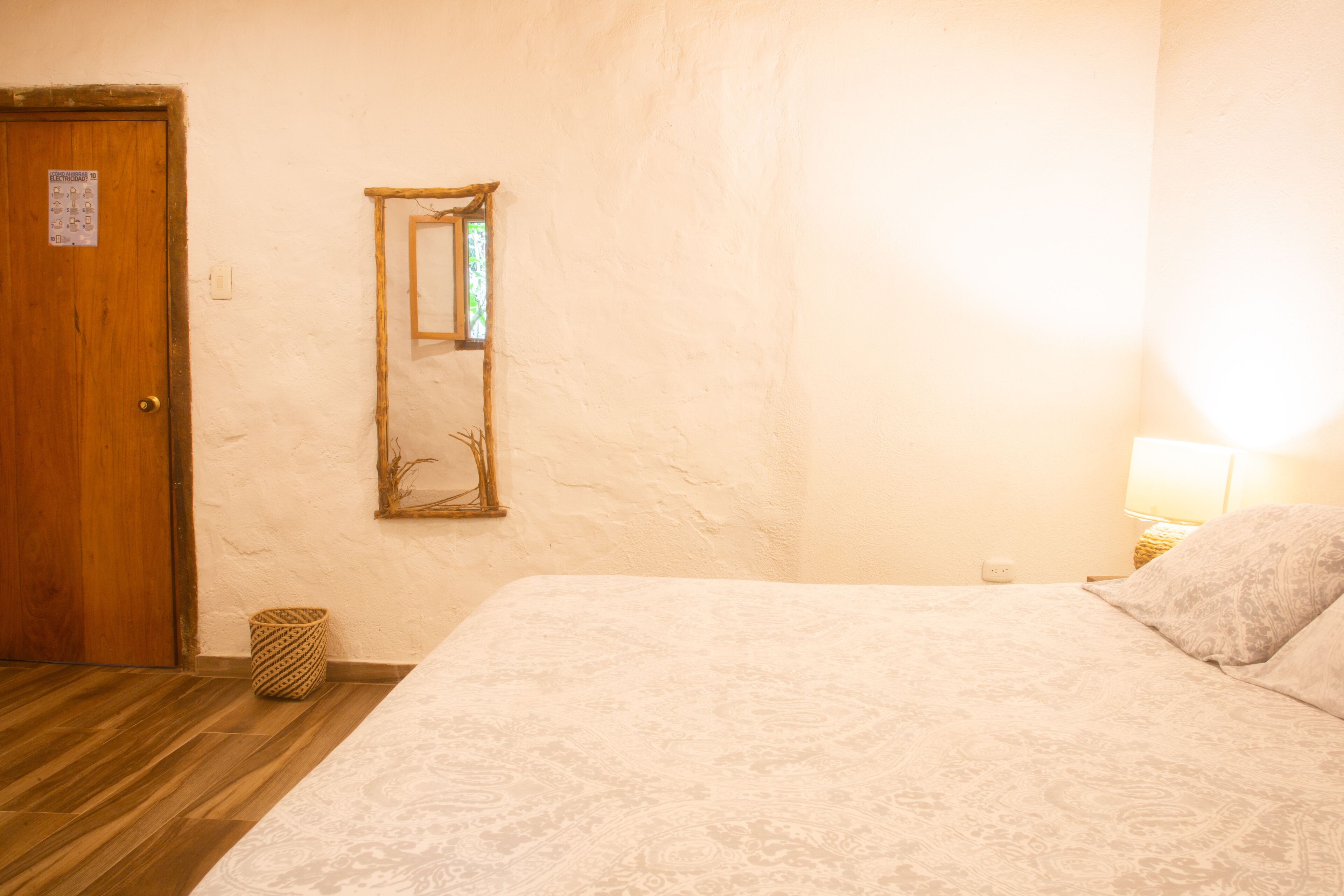 Een slaapkamer met een houten deur, een spiegel, een bedlampje en een bed met een decoratief dekbed.