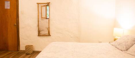 Quarto com porta de madeira, espelho, abajur e colcha estampada.