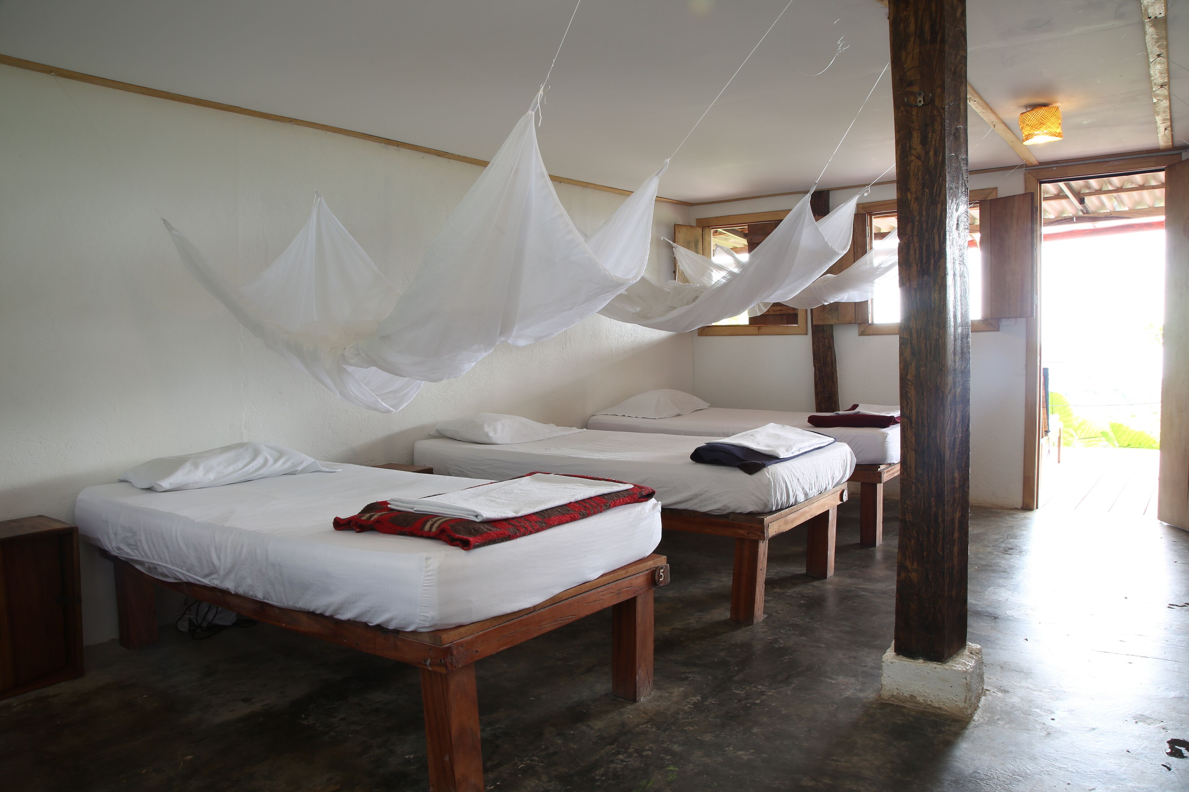 Quarto com duas camas de madeira, cada uma com roupa de cama branca e manta vermelha.