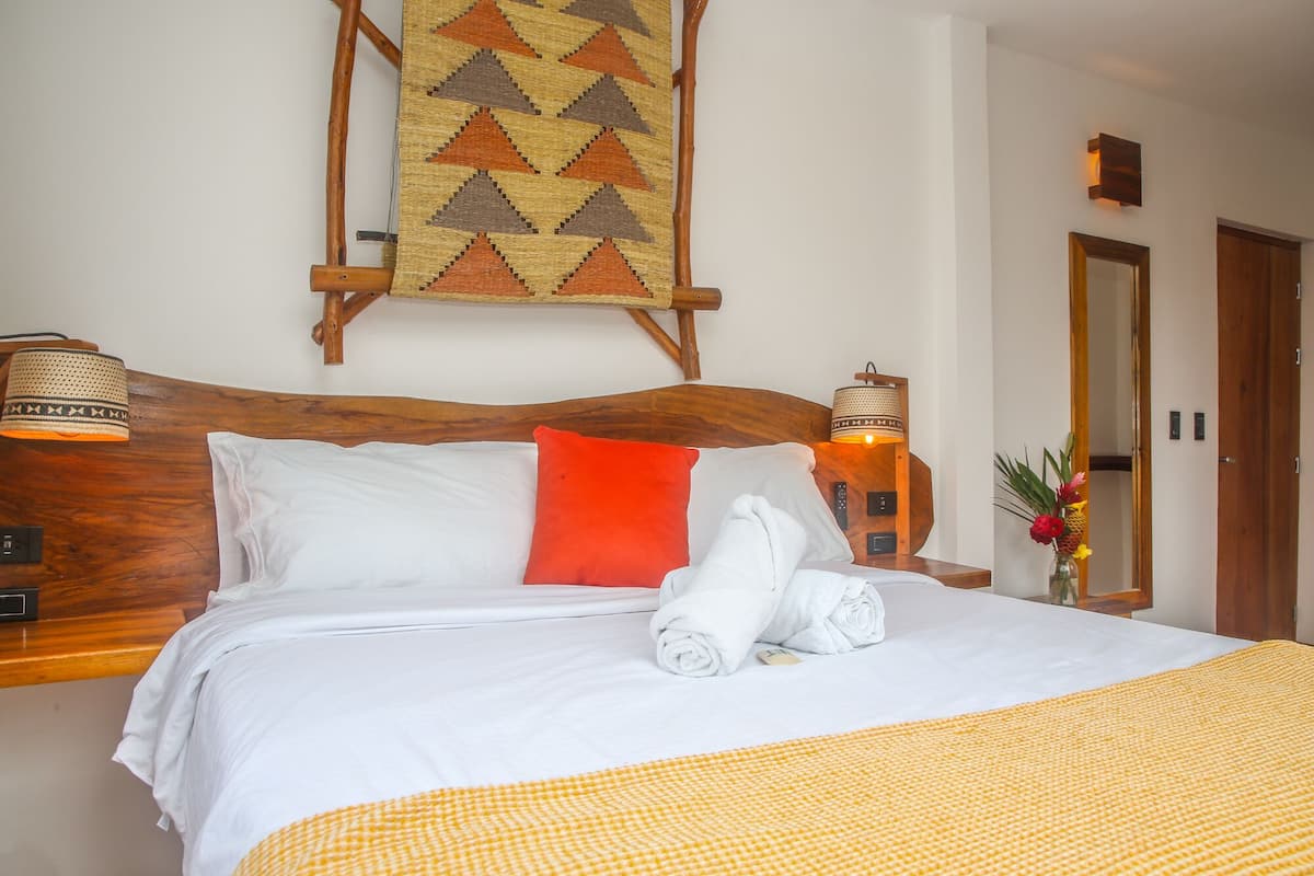 A neatly made bed with white and orange bedding, a wooden headboard, and a wall-mounted tapestry.
