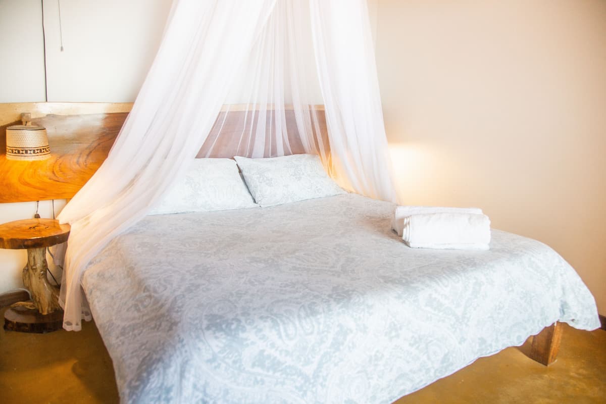 A bed with a canopy, a bedside table with a lamp, and a small wooden stool.