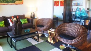 A living room with a sofa, two wicker chairs, a coffee table, and a bookshelf. - B10: 1 bedroom, 3rd floor, oceanview (Princeville)