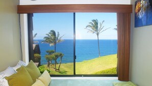 A room with a large window offering a view of the ocean and palm trees. - B10: 1 bedroom, 3rd floor, oceanview (Princeville)