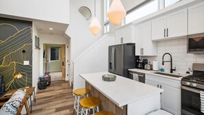 Una cocina moderna con armarios blancos, un refrigerador de acero inoxidable, horno empotrado y una isla grande con taburetes.