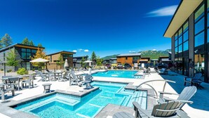 Un área de piscina con varias piscinas, sillas de descanso y edificios modernos con ventanales amplios.