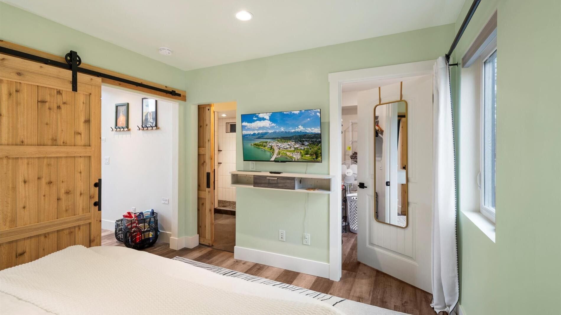 Un dormitorio con una cama, un televisor montado en la pared y vistas a un pueblo a través de una puerta abierta.