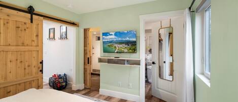 Un dormitorio con una cama, un televisor montado en la pared y vistas a un pueblo a través de una puerta abierta.