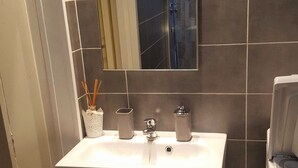 Ett badrum med ett vitt handfat, en spegel och en duschhörna.