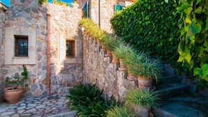 Un bâtiment en pierre, orné de pots en terre cuite disposés verticalement le long du mur, un chemin pavé et un escalier menant à l’étage supérieur.
