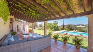 Une terrasse couverte avec une piscine, des meubles en osier et une vue sur le paysage.