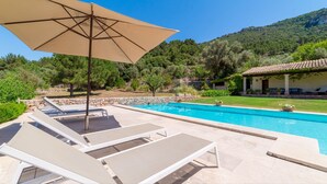 Une piscine entourée d’un mur de pierre et de verdure, agrémentée de chaises longues et d’un parasol, avec une montagne en toile de fond.