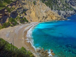Un paisaje costero con una playa, aguas azules cristalinas y acantilados rocosos.