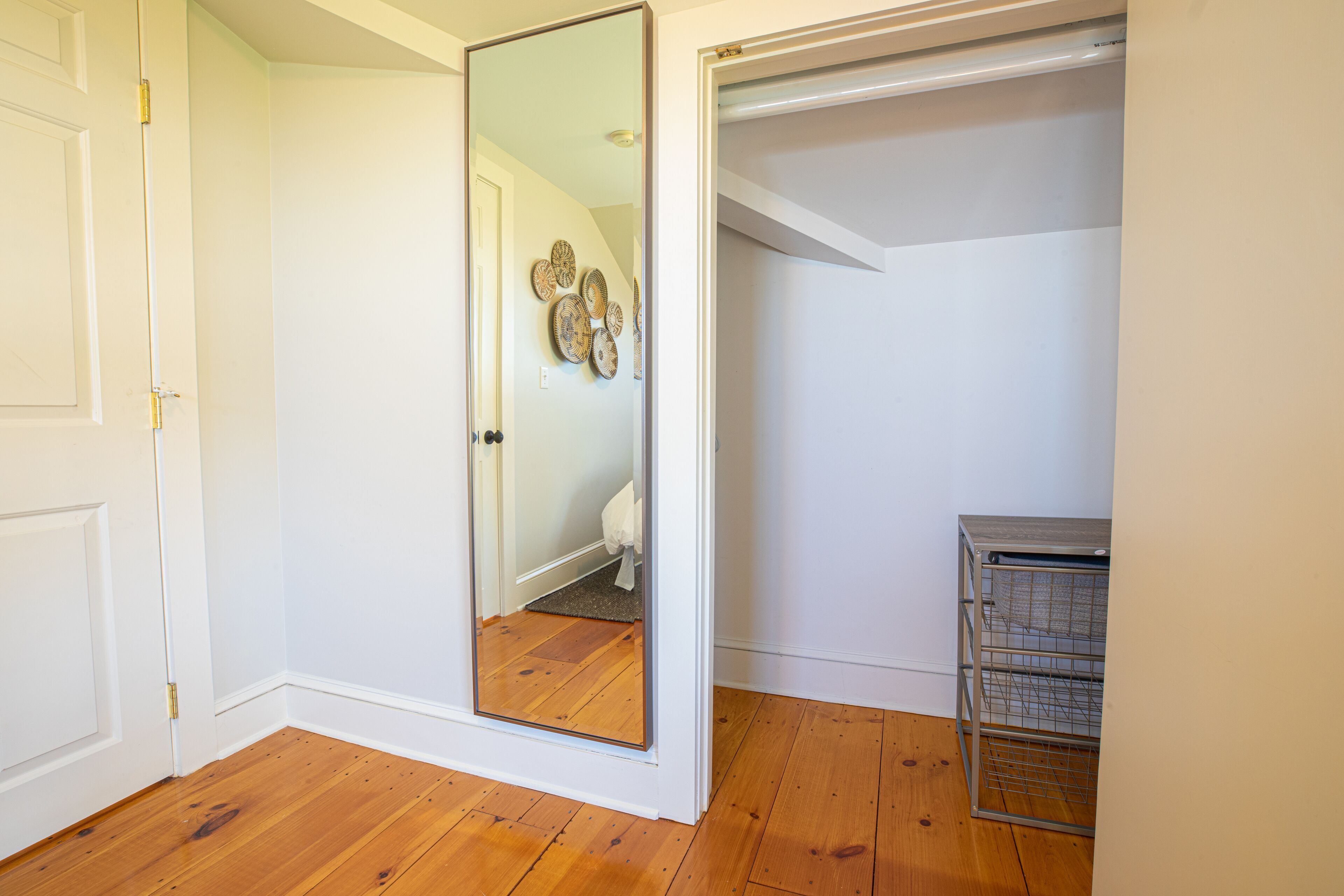 A room with a wooden floor, a white door, a mirror, and a metal storage unit.