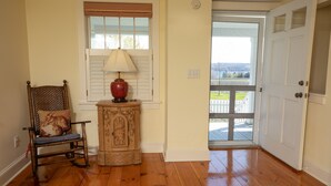 A wooden floor, a rocking chair with a cushion, a lamp, a cabinet, and a door leading to a balcony. - North Cottage at Hobbit Hollow Farm (Skaneateles)