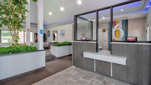 A modern reception area with a reception desk, a large mirror, and a plant. - Studio 6 Georgetown, KY – Lexington North (Georgetown)