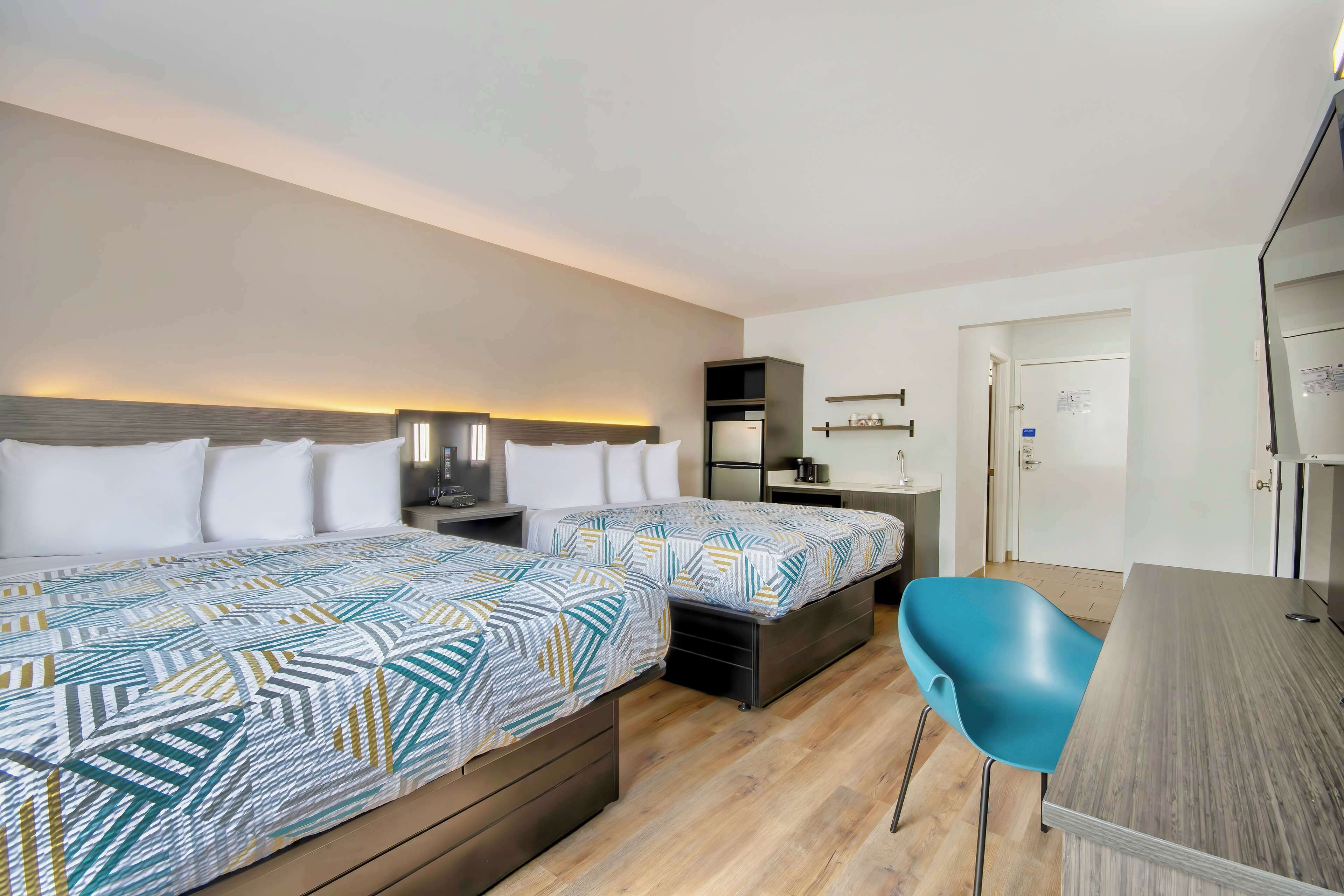Una habitación de hotel con dos camas, un escritorio, una silla azul y un armario.