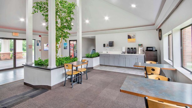 A modern indoor space with a reception area, seating arrangements, a kitchen area, and large windows providing natural light. - Studio 6 Georgetown, KY – Lexington North (Georgetown)