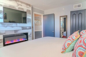 A bedroom with a fireplace, a bed with colorful pillows, a wardrobe, and a mirror.