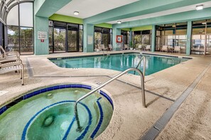 An indoor swimming pool with clear water, a diving board, and lounge chairs.