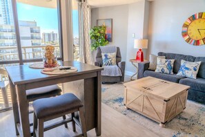 A modern living room with a dining table, a sofa, a coffee table, and a large window with a view of buildings.