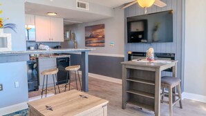 A modern kitchen with a bar area, a ceiling fan, and a flat-screen TV. - Meridian 705 (Myrtle Beach)