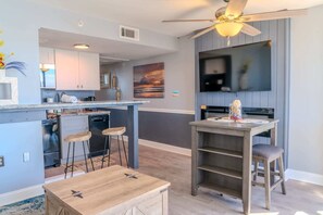 A modern kitchen with a bar area, a ceiling fan, and a flat-screen TV. - Meridian 705 (Myrtle Beach)