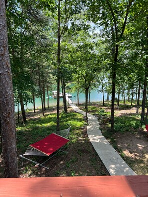 A hammock and a red mat in a wooded area with a path leading to a body of water.