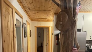 A wooden interior with a rustic tree trunk centerpiece, a hallway leading to a bedroom, and a refrigerator in the background. - THIRTEEN FEET of water at our dock currently SUPER CUTE On the lake, Deep Water  (Hartwell)
