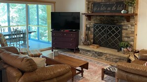 A spacious living room with a stone fireplace, leather sofas, a flat-screen TV, and a dining area with a large window. - THIRTEEN FEET of water at our dock currently SUPER CUTE On the lake, Deep Water  (Hartwell)
