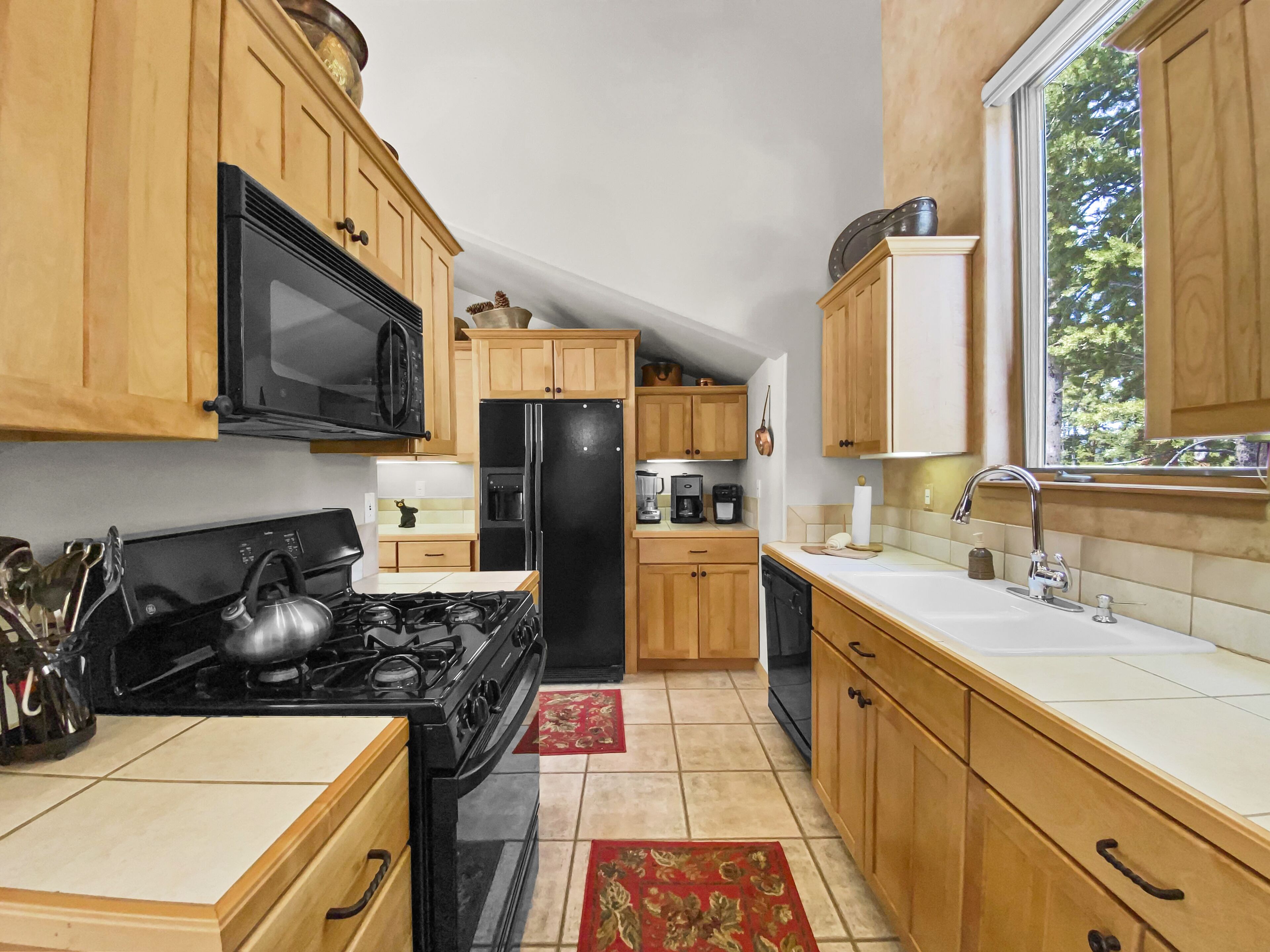 Une cuisine de taille réduite, dotée de meubles en bois, d’une cuisinière noire, d’un four à micro-ondes, d’un réfrigérateur et d’un évier.
