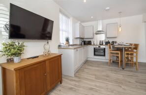 Een moderne keuken met witte kasten, een houten eettafel en een flatscreen televisie aan de muur.