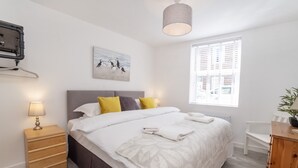 Ein ordentlich eingerichtetes Schlafzimmer mit Bett, Nachttisch, Lampe und einem Fenster mit Jalousien.
