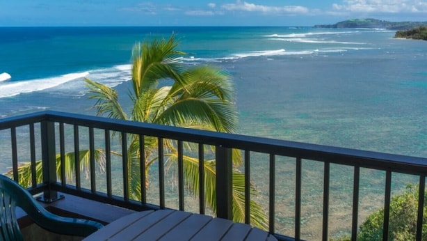 Ein Balkon mit Blick auf das Meer, Palmen und ein entferntes Land.
